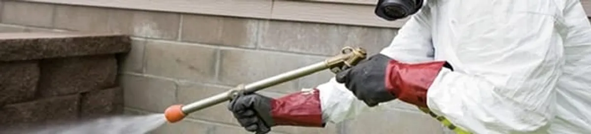 Pest control technician applying exterior insect treatment along a home foundation in Duluth, MN