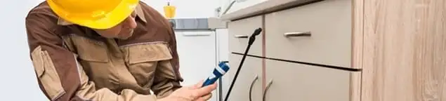 Roach exterminator applying treatment under kitchen cabinets in Duluth, MN