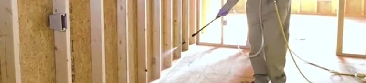 Termite treatment technician applying spray along framing and unfinished walls in Duluth, MN